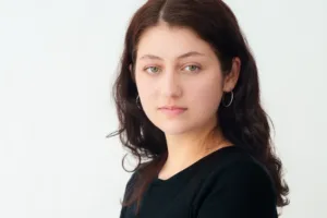 A close-up portrait of a woman with natural makeup and hoop earrings, photographed in soft natural light for a clean and elegant look by JG.