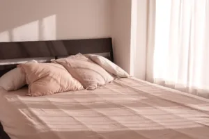 A bedroom filled with natural light. Muted linens and a wooden headboard.