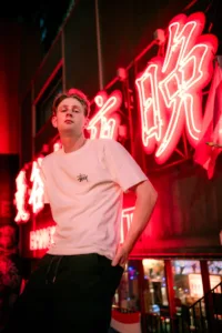 Portrait éclairé au néon dans une ruelle de Shibuya la nuit, avec des enseignes lumineuses, par JG.