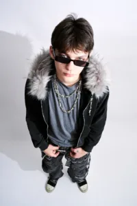 High-angle portrait of a model in a Post Xeno faux-fur hooded jacket and barbed wire necklaces, by JG.