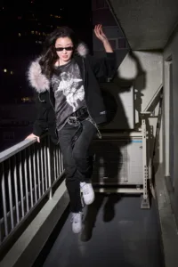 Model in a Post Xeno fur-lined hoodie and studded belt on a Shibuya balcony at night.