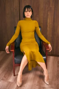 Model in a mustard yellow turtleneck dress and heels seated in a black leather armchair at a Tokyo studio.