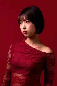 Beauty portrait of a model with a short bob in a red lace off-the-shoulder dress against a deep red background, by JG in Tokyo.