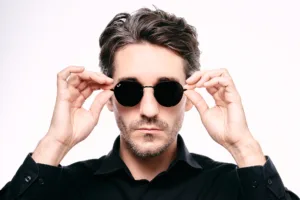 High-contrast self-portrait of JG in round black Ray-Ban sunglasses against a white background.