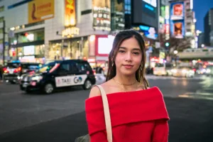 Séance photo portrait à Shibuya de nuit, femme en pull rouge épaules dénudées avec les néons et la circulation de Tokyo en arrière-plan : tour photographique JG Studio Tokyo.