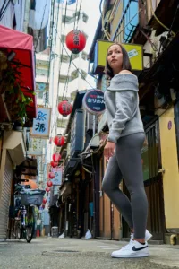 Portrait d'une femme regardant par-dessus son épaule dans une ruelle étroite d'un yokocho à Shibuya, ornée de lanternes rouges, par JG.